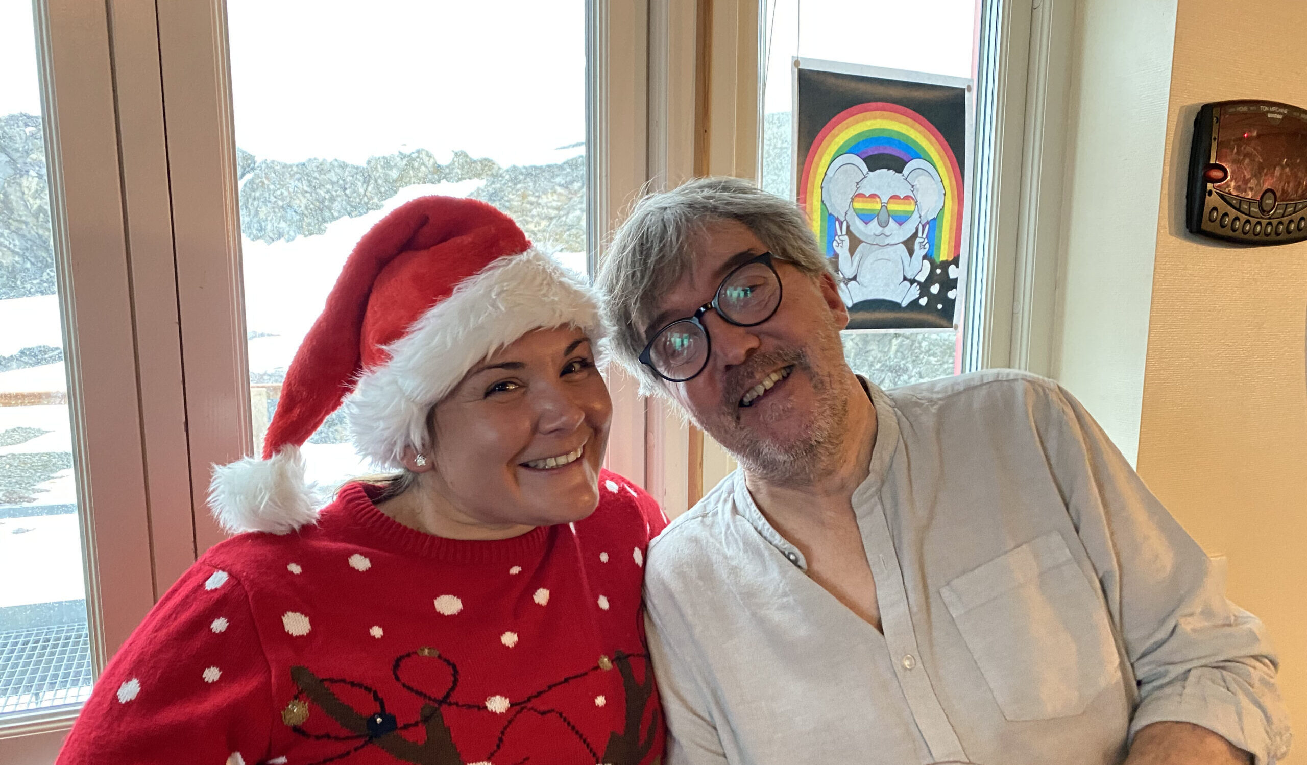 A man with glasses and a woman wearing a Christmas jumper and a Santa hat smiling at the camera